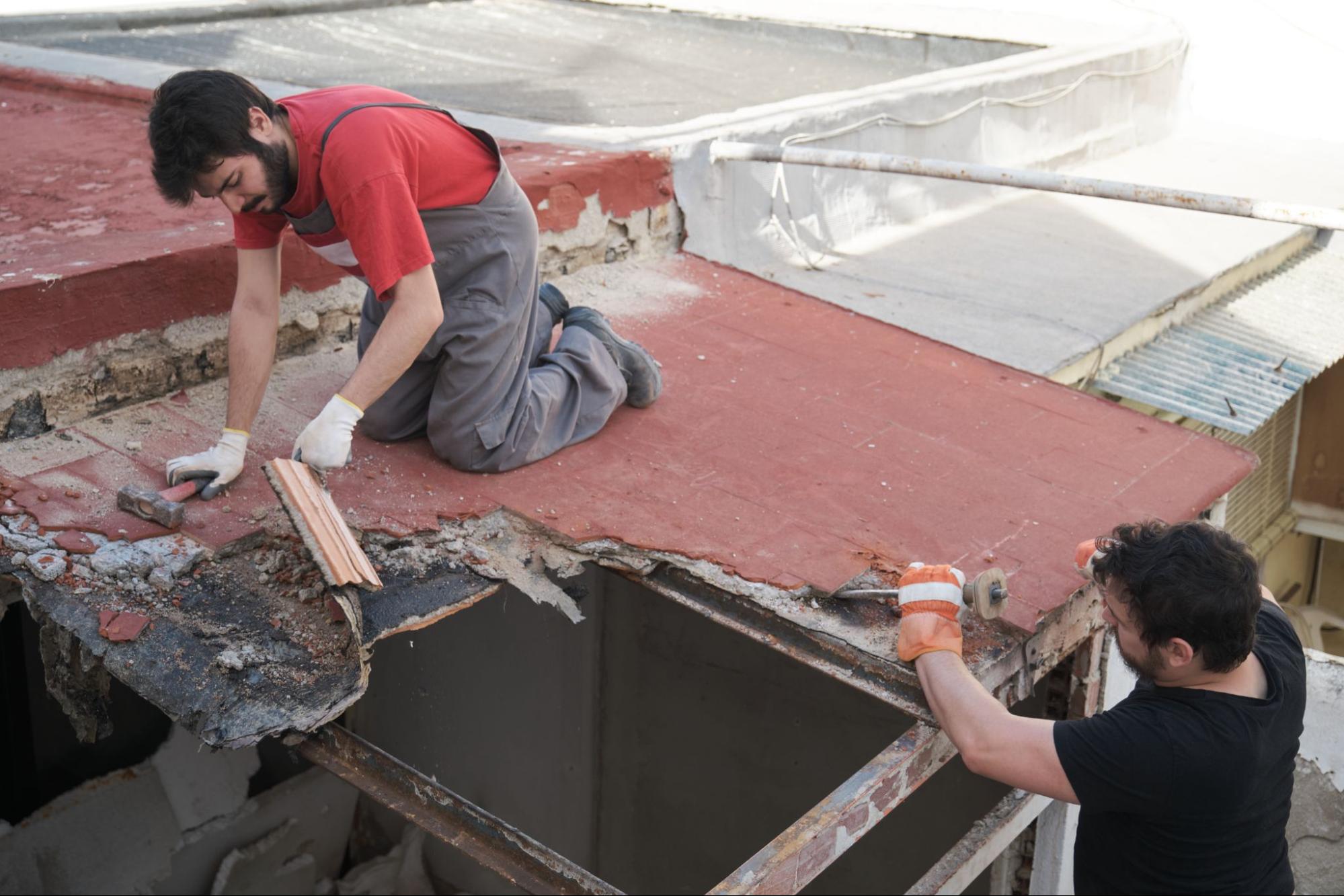 Two masons working on a roof replacement, tearing down the old ceiling structure of a house.