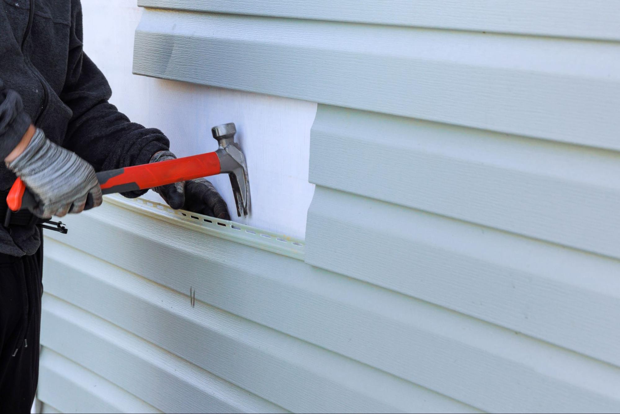 A close-up of a worker's hands holding a hammer during siding replacement.