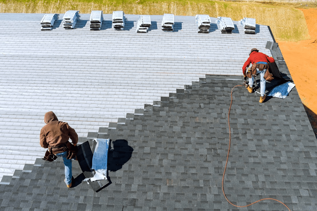 An aerial view of two workers replacing shingles on a roof.