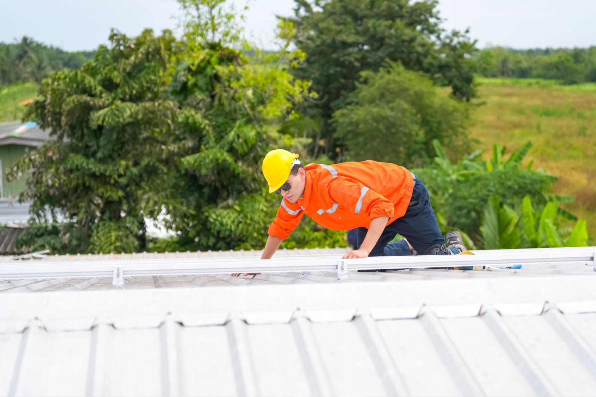 Roof maintenance crew in safety gear inspecting gutters on a rooftop.