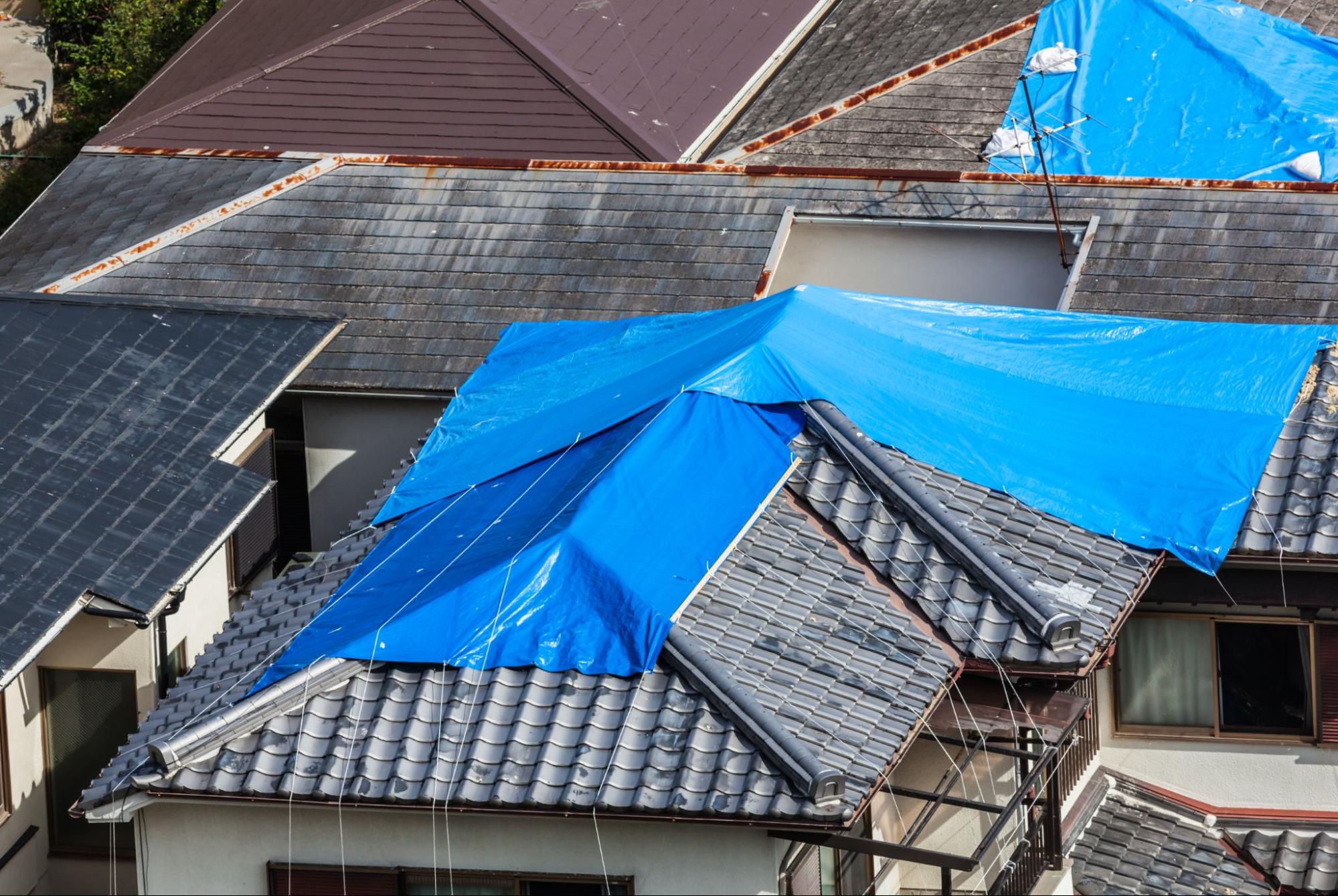 Residential homes with damaged tile roofing secured with blue tarps