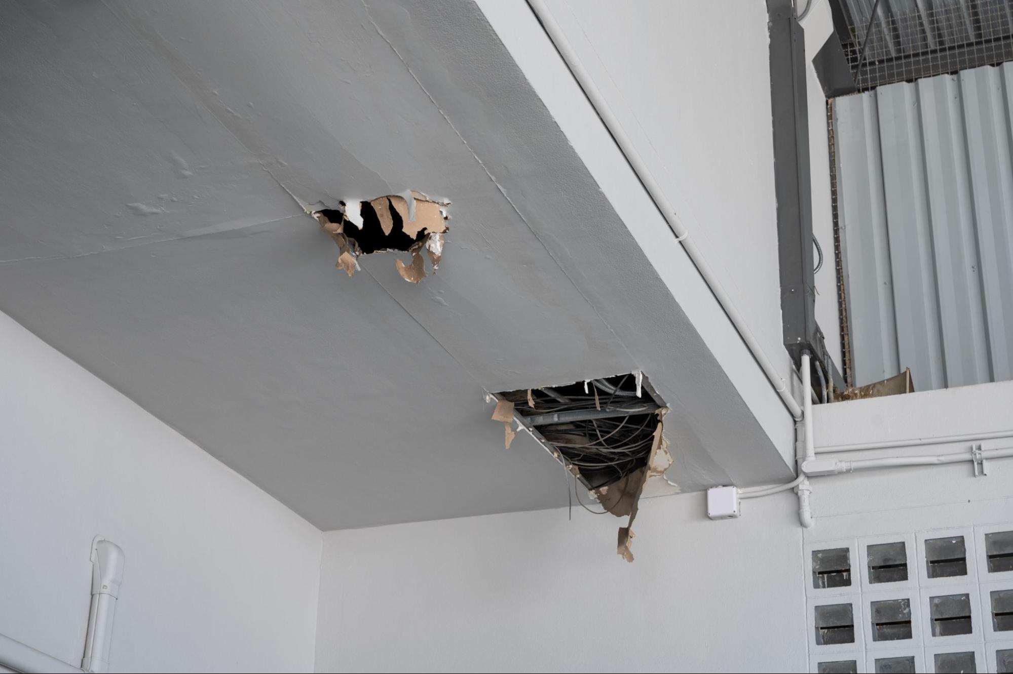 Ceiling panel with a crack and hole exposing wires, damaged by water leakage from neglected gutter maintenance.