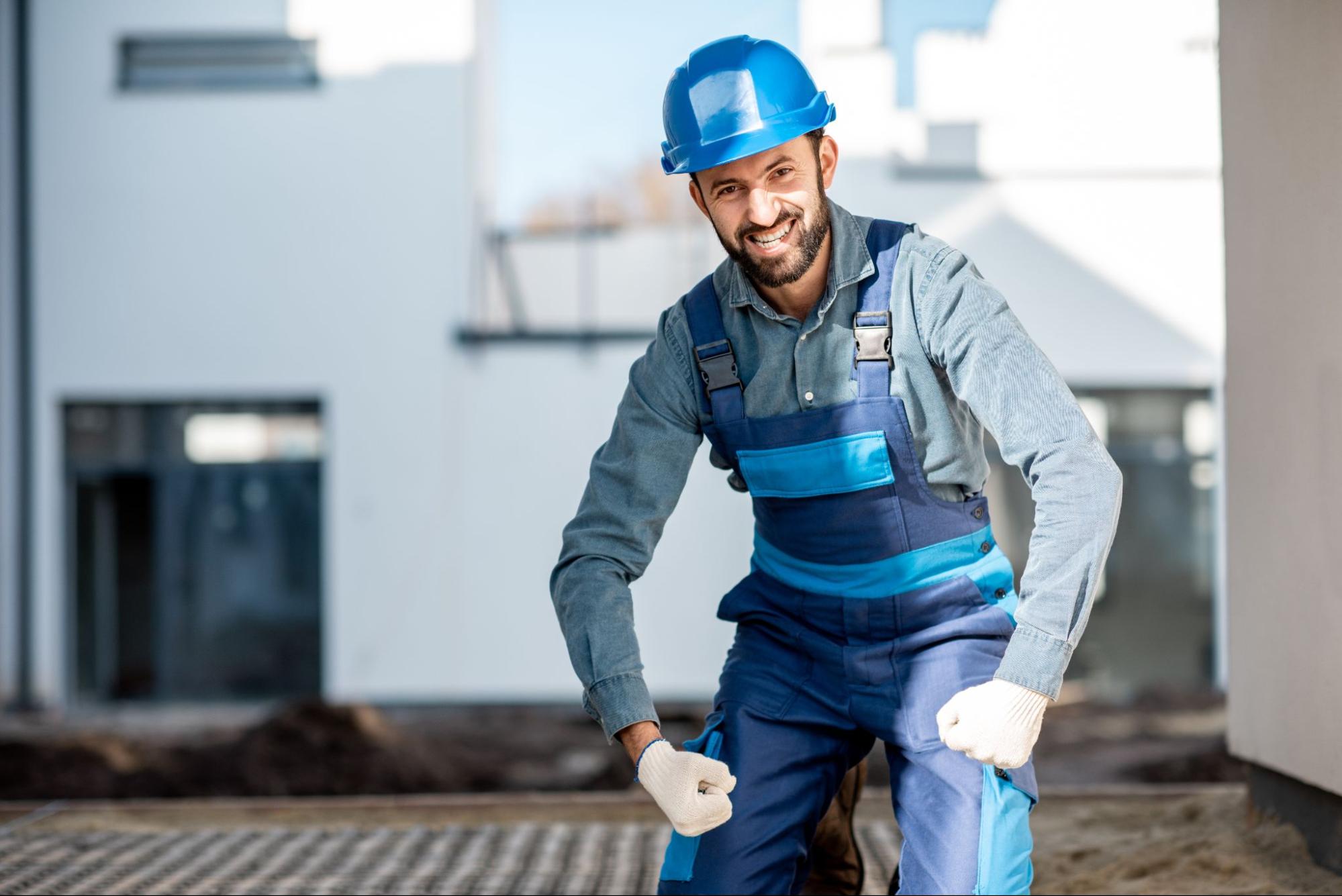 A roof repair specialist in a blue hard hat smiles at the camera after finishing his task.