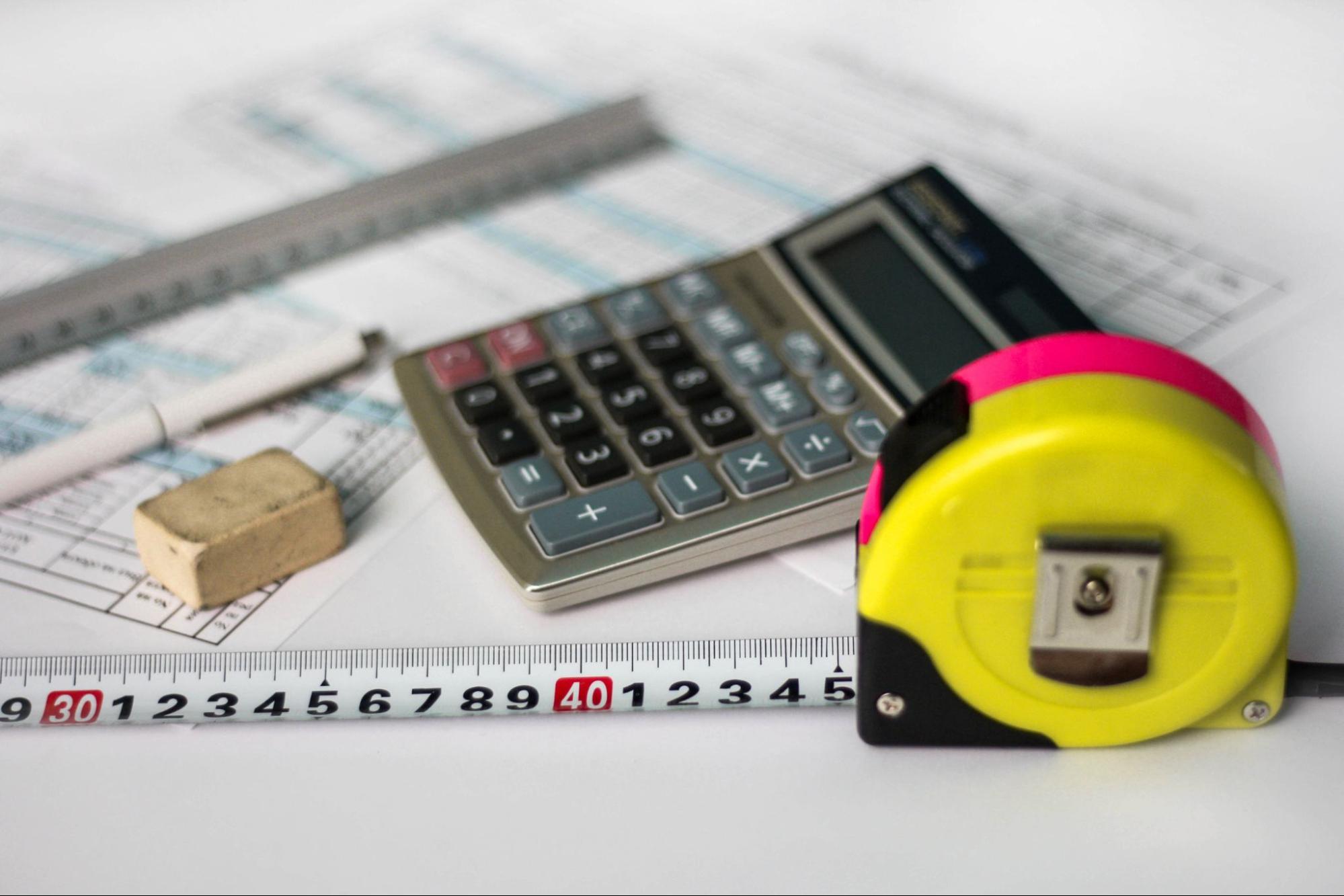 Calculator, measuring tape, ruler, pen, and paperwork on a table. 