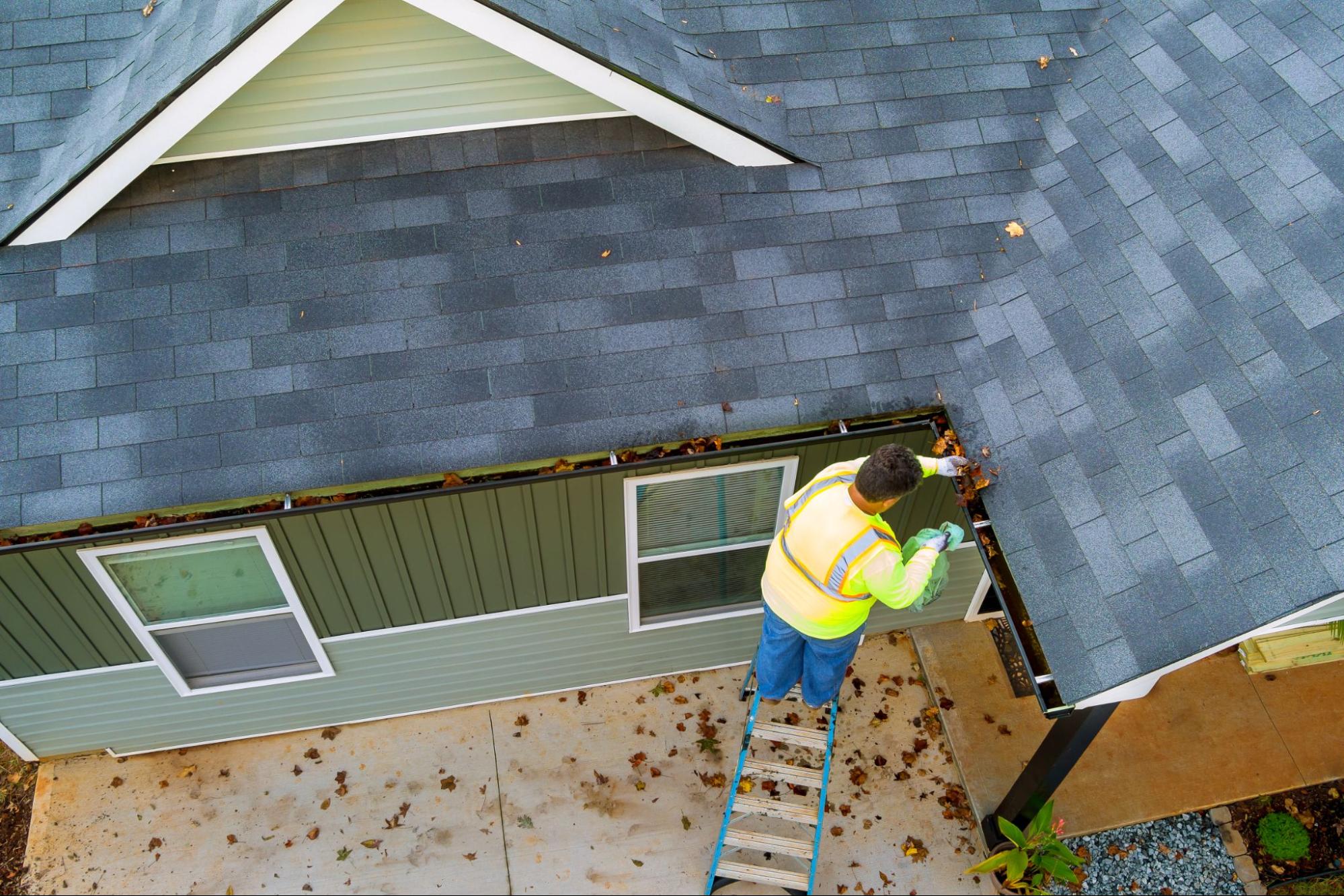 Top view of a worker clearing debris from a clogged roof gutter drain during maintenance.