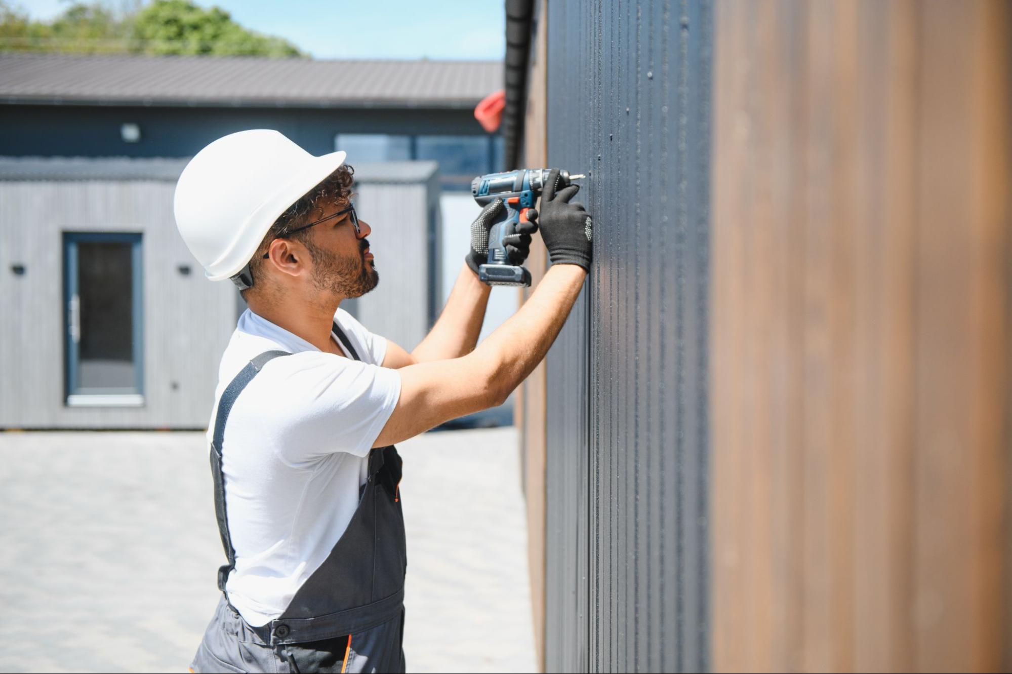 An installer fastens the siding panels with a cordless drill on the wall of a modular home
