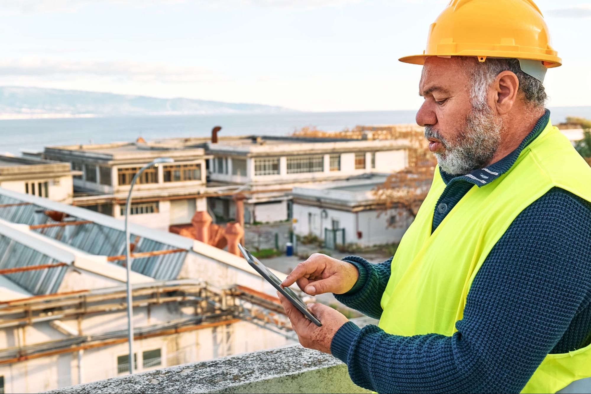 A senior roofer conducts a roofing inspection in an industrial area using a tablet
