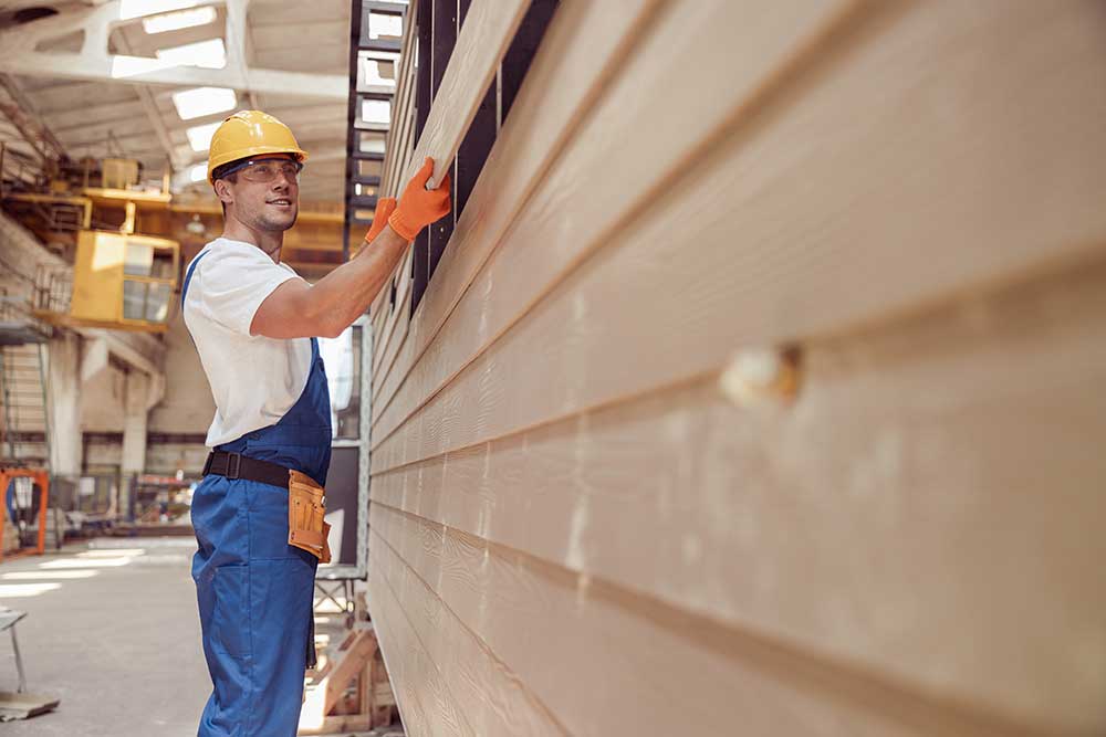 Worker in hard hat and gloves inspecting machinery in an industrial setting.
