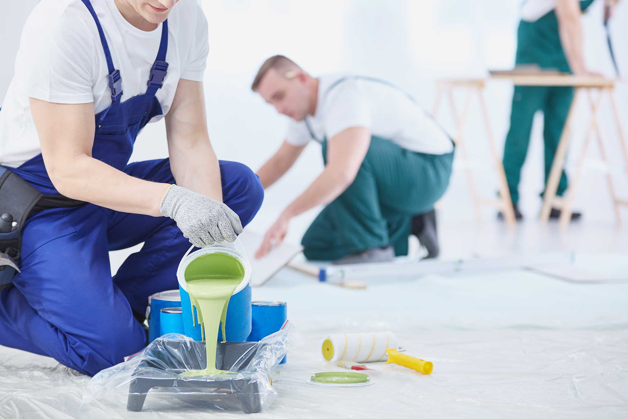 Workers in coveralls preparing paint and rollers for house renovation.