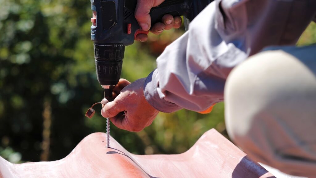 Close-up of a roofer’s hand securing a metal roofing panel with a power drill