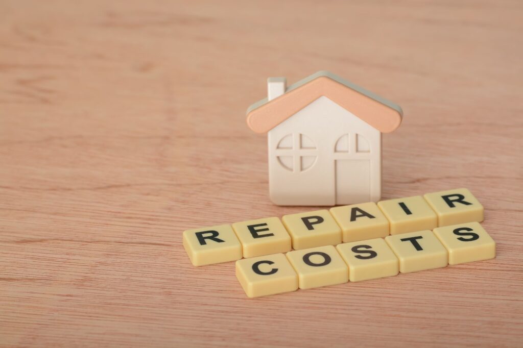 A miniature home with the words “repair costs” spelled in Scrabble tiles