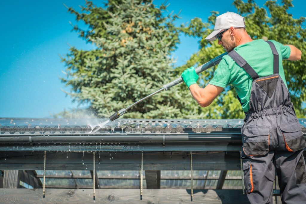 A service crew using a power hose safely cleans the roof and gutters.