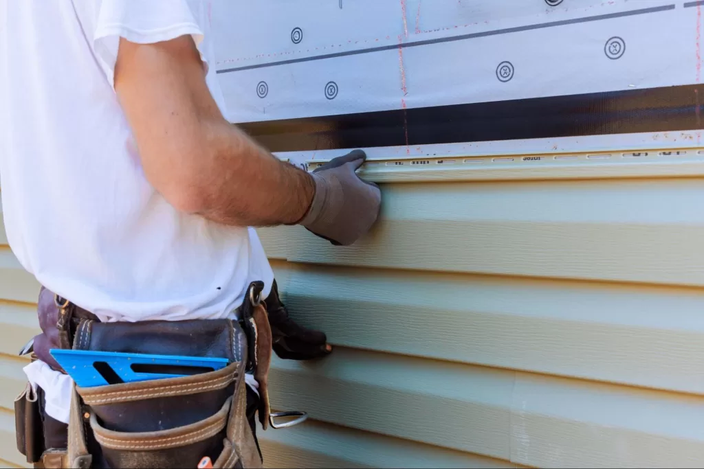 A cropped shot of a handyman installing vinyl siding on the exterior wall of a new home.