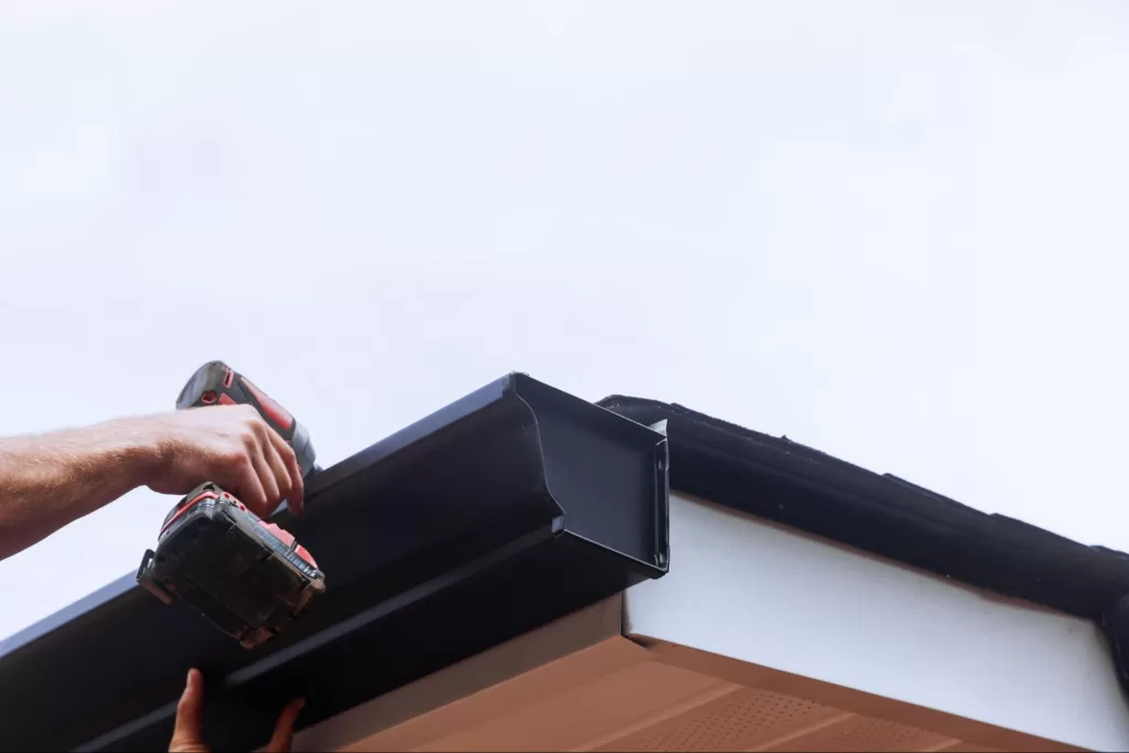 Worker installing rain gutter system mounts downpipe to a roof edge.